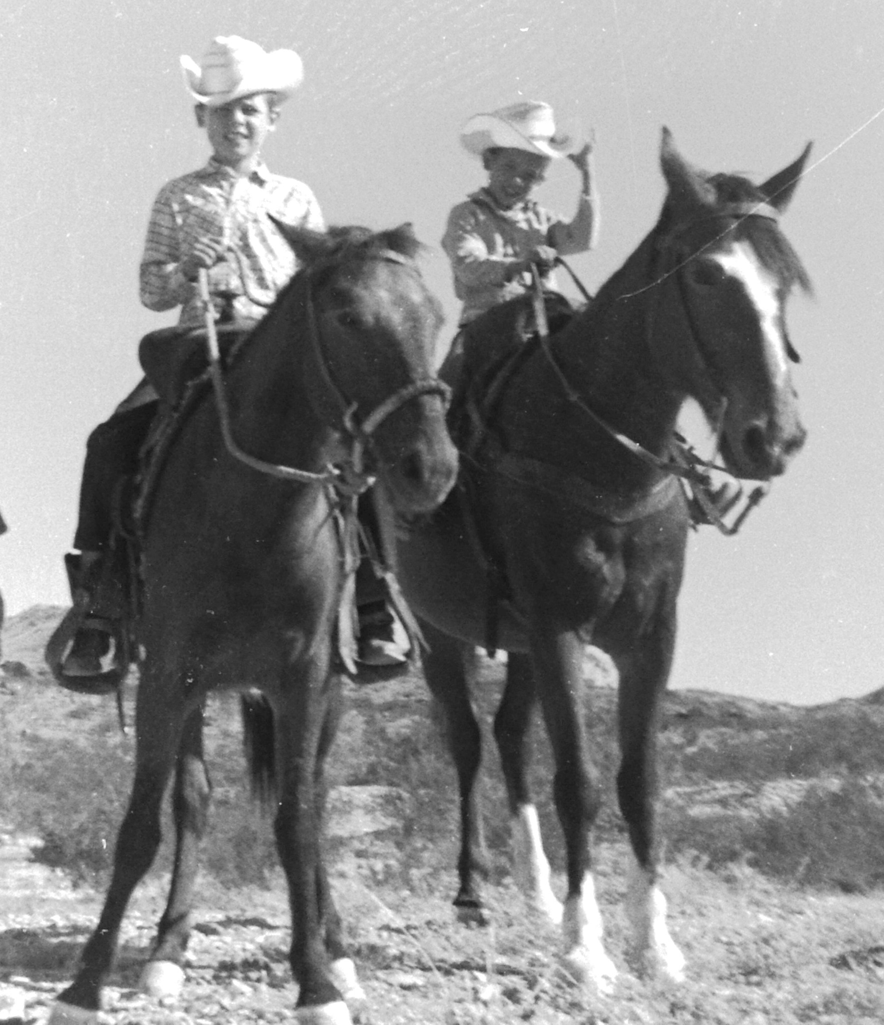 Black and white photo of two young boys in cowboy hats riding horses.
