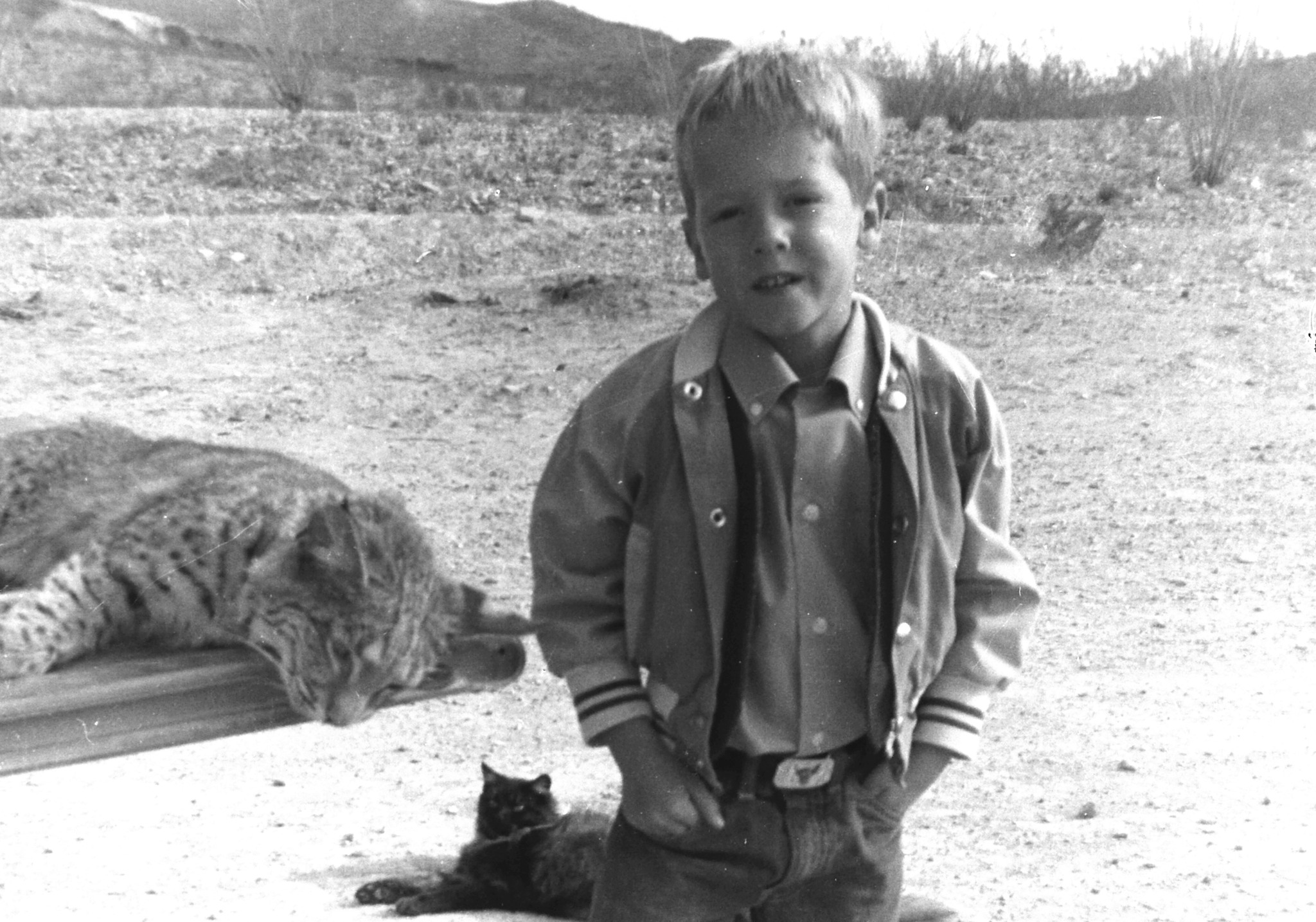 Black and white photo of a young boy looking directly at the camera, with desert scenery behind him.